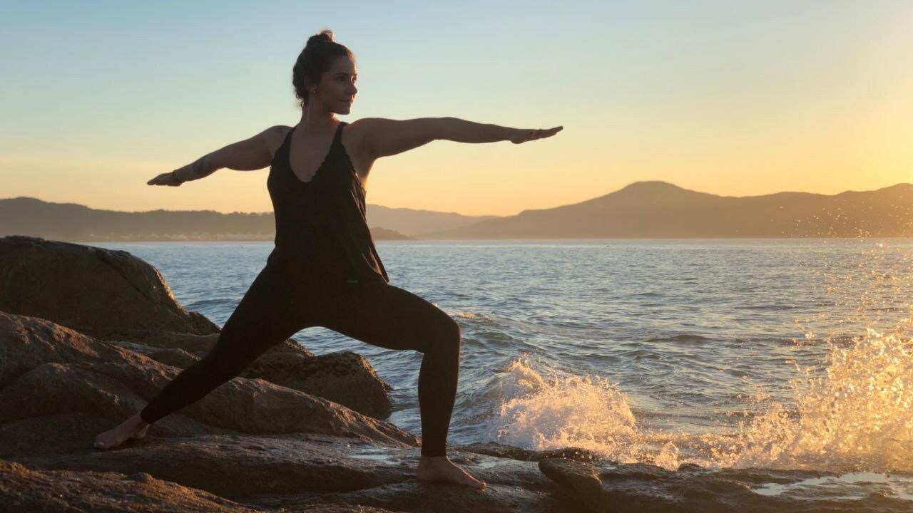 Dani Pinotti em postura de guerreiro durante prática de yoga ao entardecer, inspiração para aulas online de qualquer lugar.
